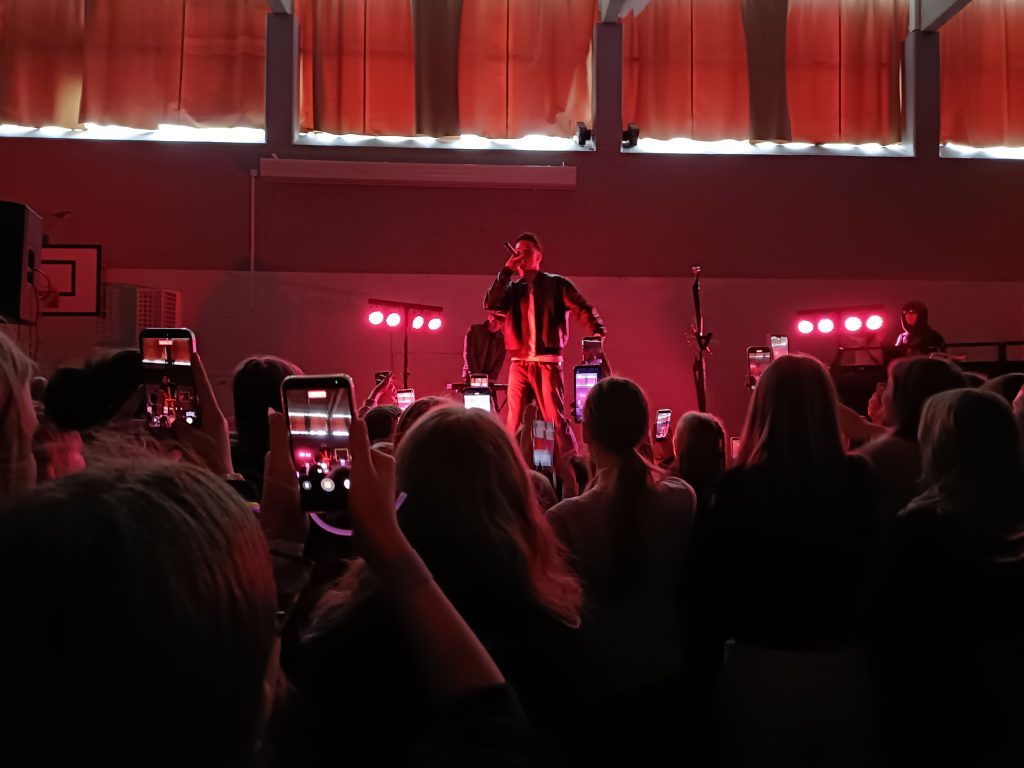 Rap-artisti esiintyy ja yleisö kuvaa esitystä puhelimillaan.