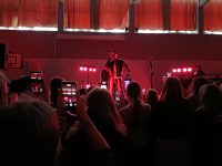 Rap-artisti esiintyy ja yleisö kuvaa esitystä puhelimillaan.