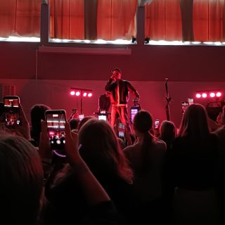 Rap-artisti esiintyy ja yleisö kuvaa esitystä puhelimillaan.