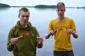 Nuoret miehet seisovat järven rannalla, molemmilla vaaput käsissään.